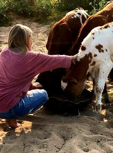 Woman petting a calf while it drinks.