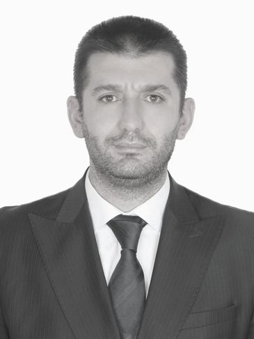 Serious man in a formal suit and tie against a plain background.