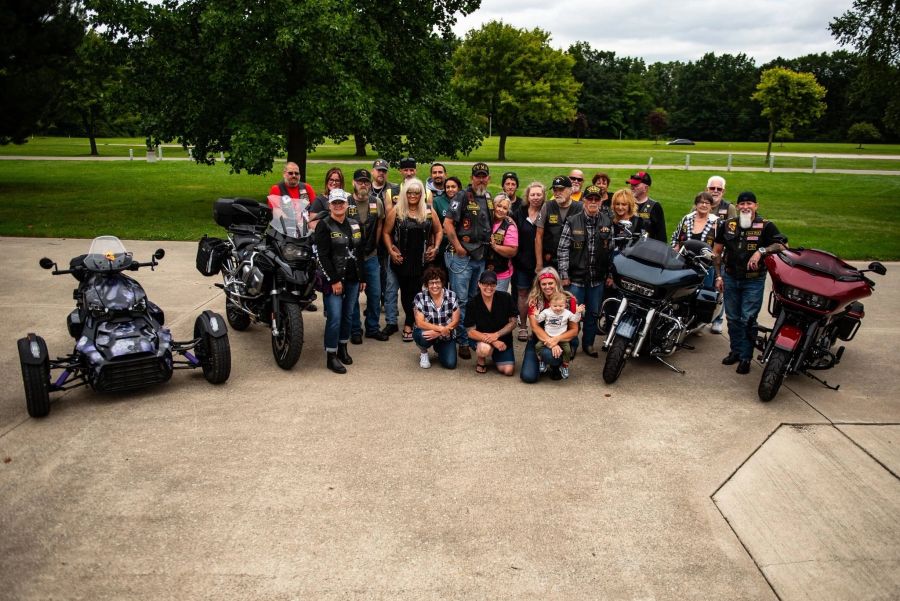 Members posing with their motorcycles and a trike in a park