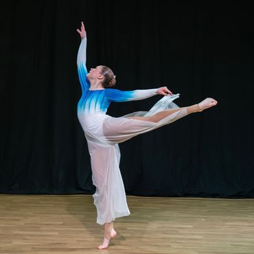A ballerina in a flowing dress performs an elegant arabesque on stage.