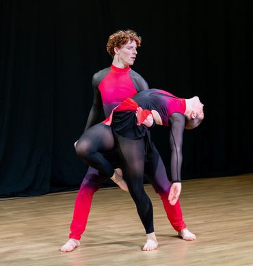 Two dancers in black and red costumes performing a dramatic pose on stage.