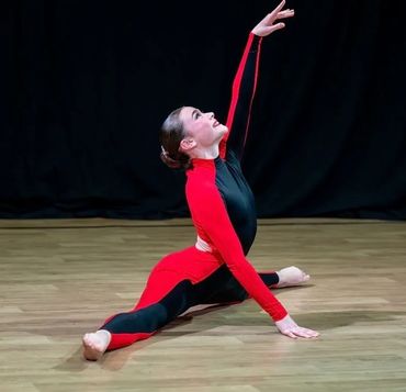 Dancer in red and black outfit performing a split with an elegant arm pose.