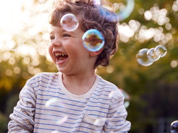 Happy child laughing amidst soap bubbles outdoors.