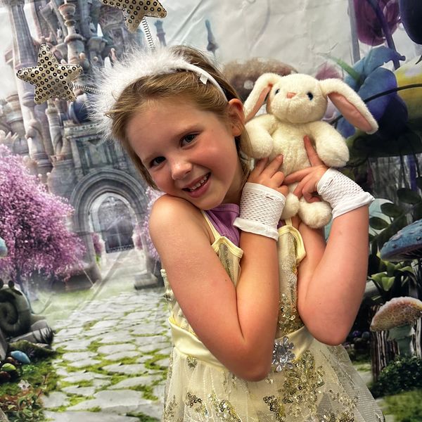 Smiling girl in princess costume holding a stuffed bunny.