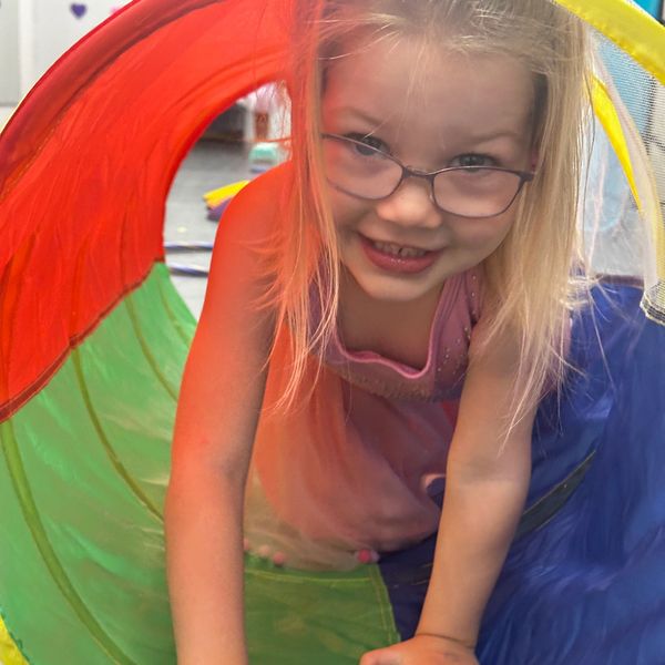 Smiling girl crawling through a colorful play tunnel.