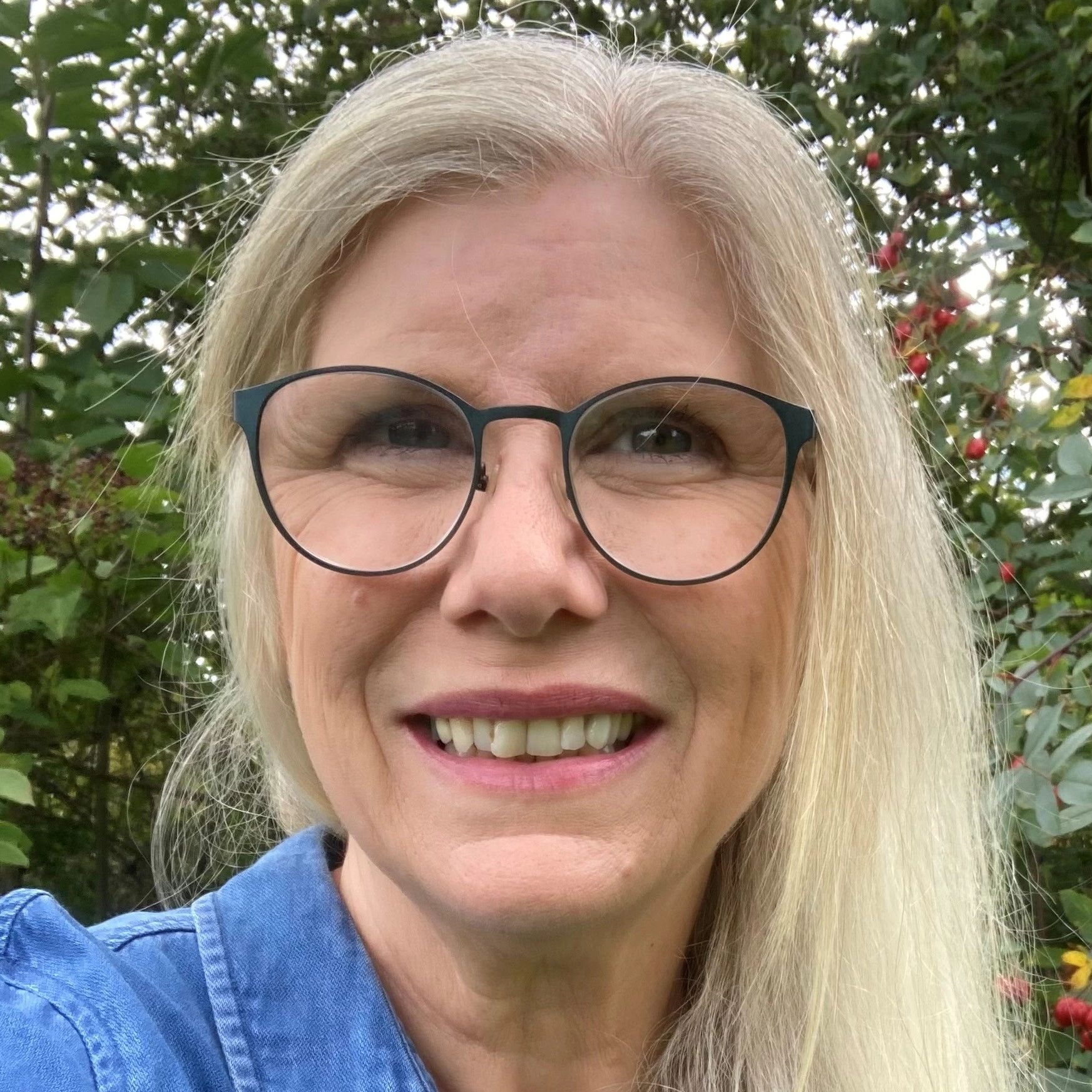 A photo of Jen with long blond hair, wearing glasses and smiling at the camera. 