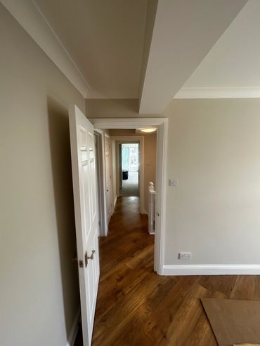 Hallway with open white door and wooden floor.