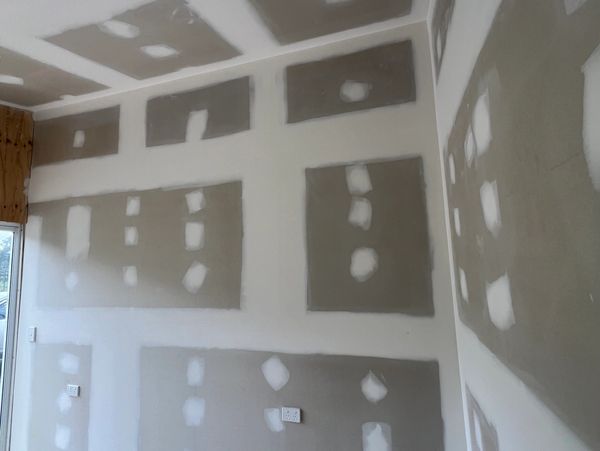 Drywall installation with visible joint compound patches in an unfinished room.
