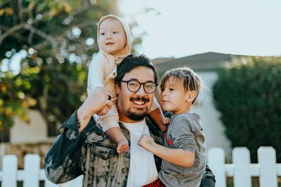 Image of dark haired man holding infant child on shoulders and a toddler in crook of arm