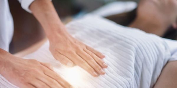 Hands performing energy healing on a person lying down.
