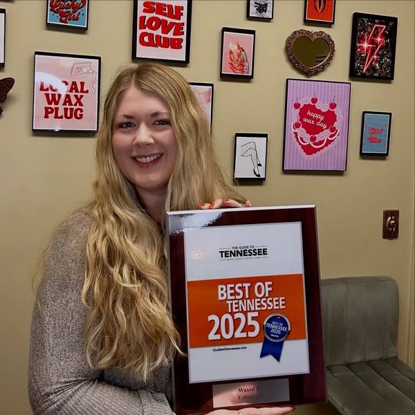 Woman holding a Best of Tennessee 2025 award plaque with a decorated wall behind her.