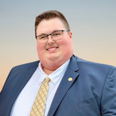 Smiling man in suit and tie with glasses outdoors.