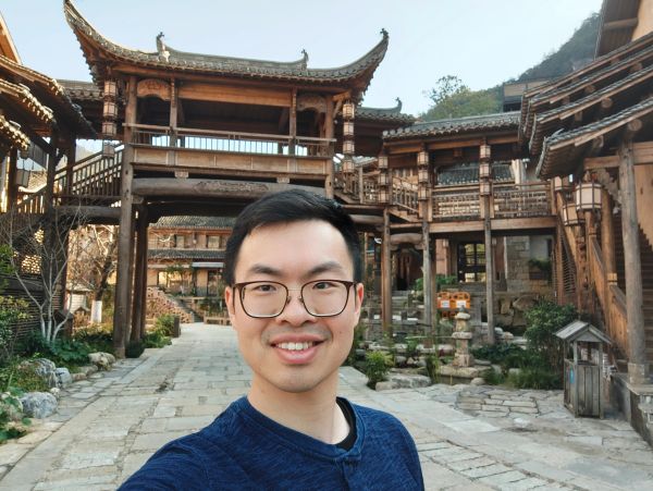 Man taking a selfie in front of traditional wooden architecture.