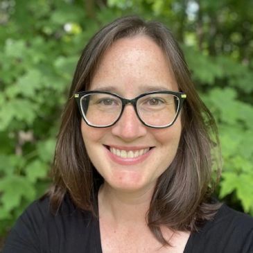 Smiling woman with glasses outdoors.