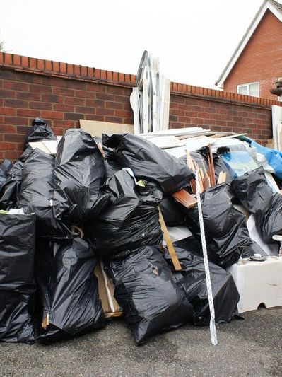 Pile of black garbage bags and debris beside a brick wall.