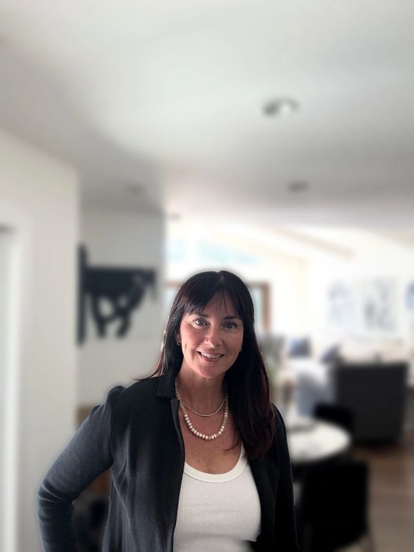 Woman smiling indoors wearing a black cardigan and white top.
