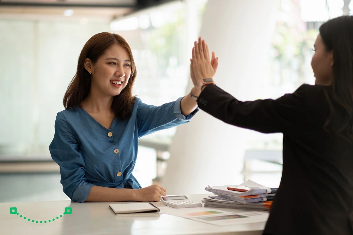 Two colleagues celebrating success with a high-five in a modern office, representing teamwork.