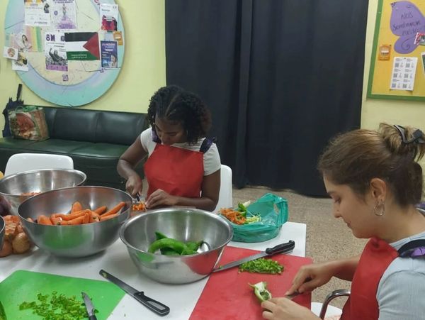 Dos personas cortan verduras en un ambiente cerrado.