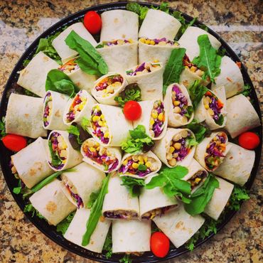 A colorful platter of vegetable wraps garnished with greens and cherry tomatoes.