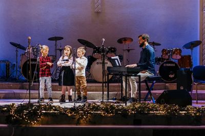 Children singing on stage with a pianist at a festive event.