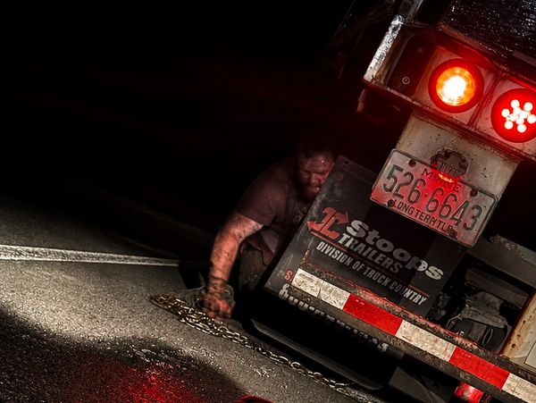 Man crawling out from under a truck at night.