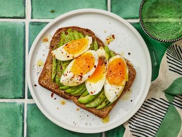 Avocado toast topped with sliced boiled eggs and seasoning on a white plate.