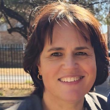 Smiling woman with short brown hair outdoors in sunlight.