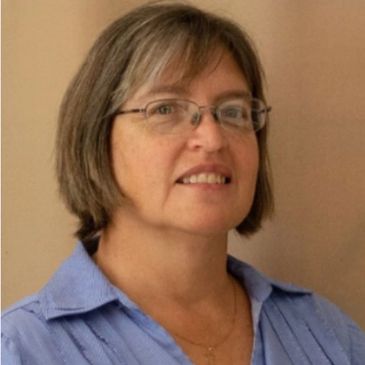 Portrait of a middle-aged woman with glasses and a blue shirt.