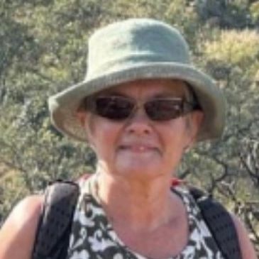 Elderly woman wearing a sunhat and sunglasses outdoors.
