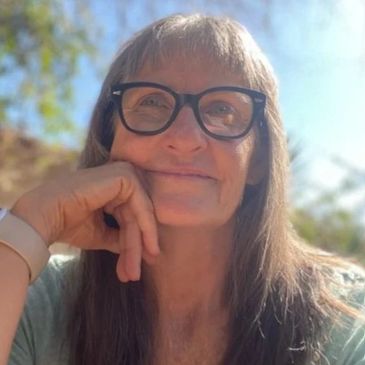 Smiling woman wearing glasses outdoors on a sunny day.
