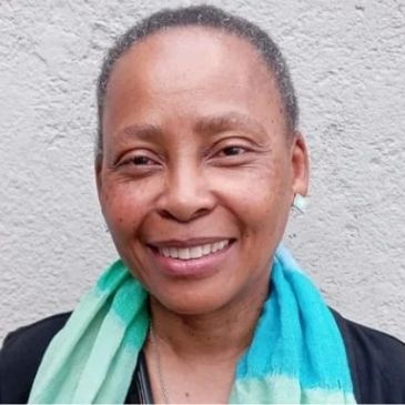 Smiling woman with a colorful scarf against a gray wall.