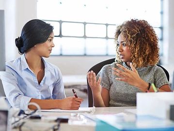 Two women engaged in a focused office discussion.