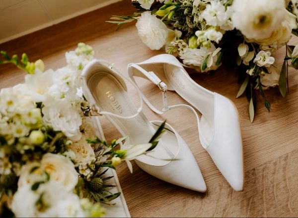 Elegant white bridal shoes surrounded by white flowers.