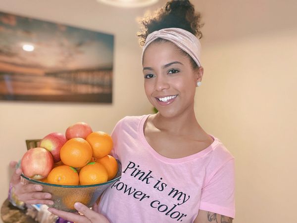 A smiling woman holding a bowl of oranges and apples.