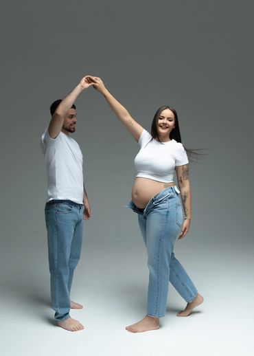Couple dancing, woman pregnant and smiling, both in casual white tops and jeans.