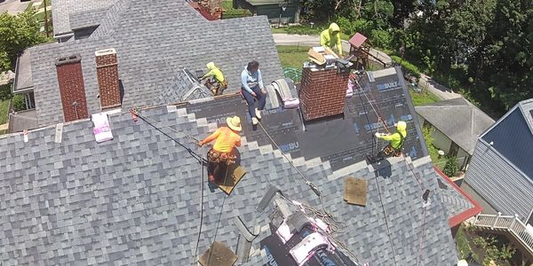 Roofers installing new grey shingles and underlayment on a residential roof.
