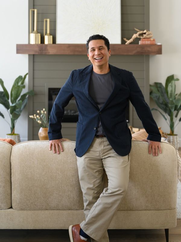 Smiling man leaning on a beige sofa in a modern living room.