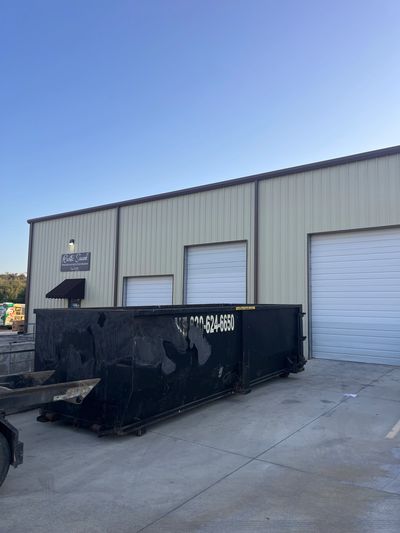 Large black dumpster in front of warehouse doors.