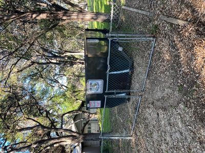 A fenced area with a large black dumpster surrounded by trees.
