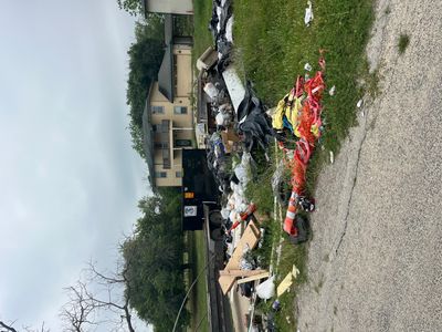 A large black dumpster surrounded by scattered trash bags and items.