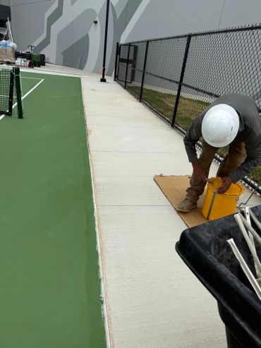 Worker in hard hat near tennis court and fence.