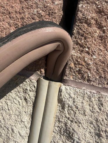 Curled rubber insulation on a cornered conduit against a textured wall.