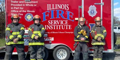 Four firefighters stand in front of an Illinois Fire Service Institute trailer.