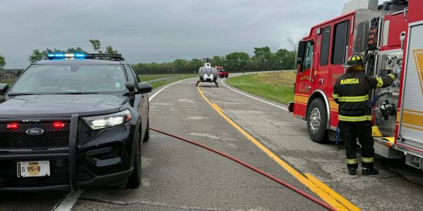 Police and fire vehicles on a roadway with emergency lights and hose.