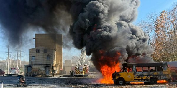 Large fire and thick black smoke from a yellow bus at emergency scene.