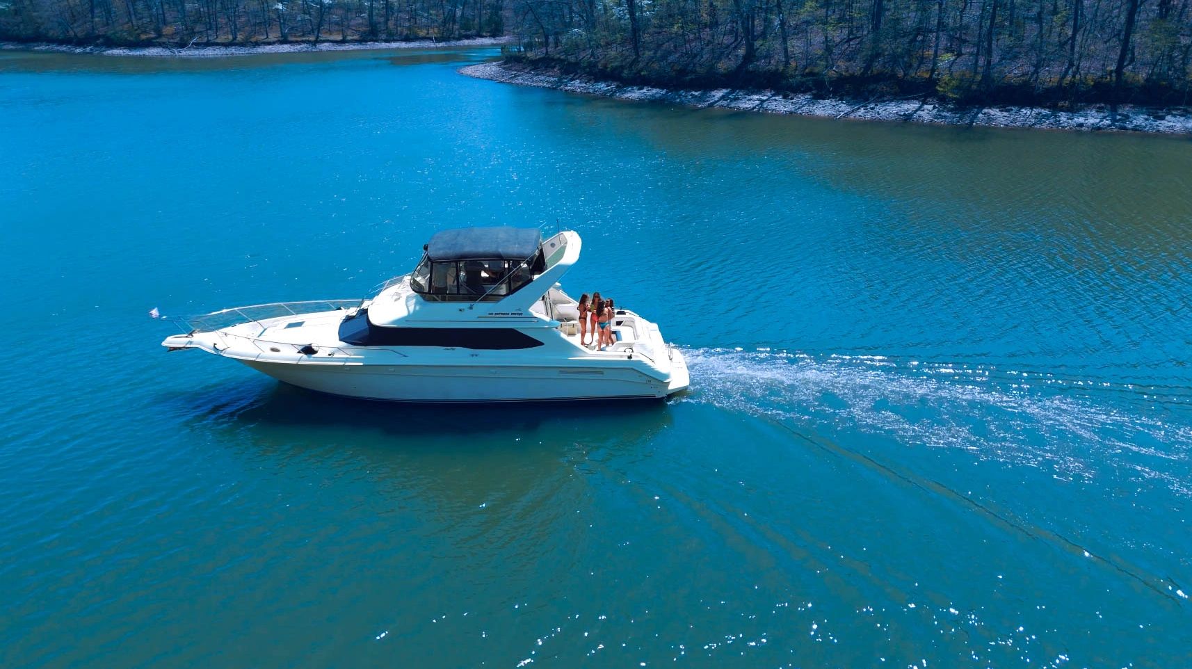 A white motor yacht with people on board cruising on a blue lake.