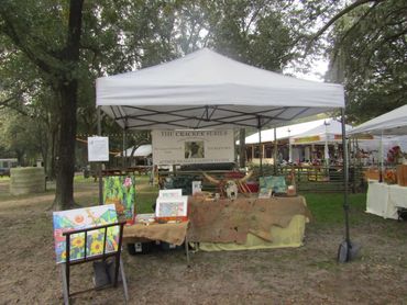 Art and book display tent at an outdoor fair with colorful paintings and rustic decor.