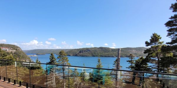 Scenic view of a lake and forest from a balcony with glass railing.