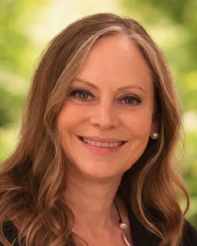 Woman smiling outdoors with green background.