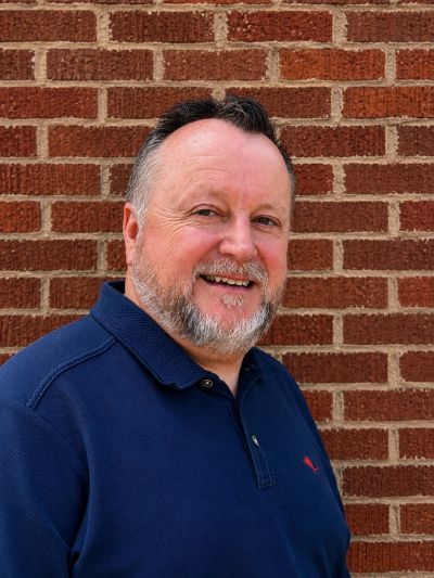 Man smiling in front of a brick wall.